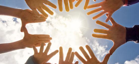 Das Bild zeigt mehrere Hände, die einen Kreis bilden, durch den die Sonne scheint.